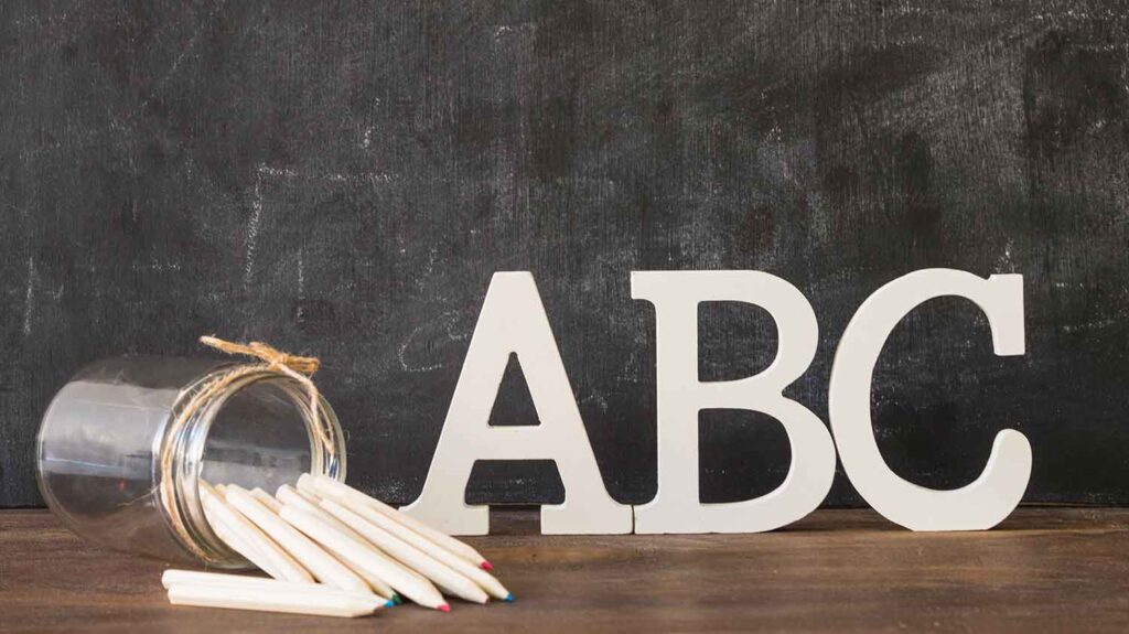 abc letters in front of a black board and pencils in front of them