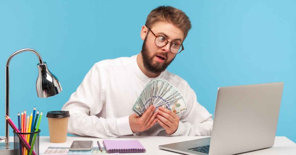 a man looking at his lap top with money in his hand