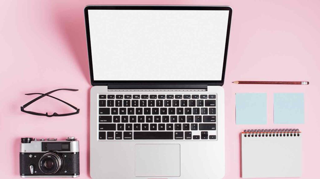 open laptop and a notebook and a camera on a pink table